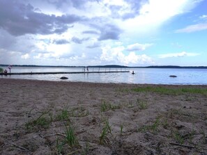 A beach with a sandy shore, a wooden pier extending into the water, and a distant tree line. - 6 Person Holiday Home in Monsteras (Monsteras)
