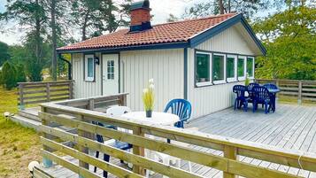 A small wooden cabin with a deck, a table, and chairs.