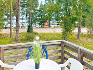 En träaltan med ett bord och stolar, med utsikt över en parkeringsplats med fordon och en byggnad i bakgrunden.