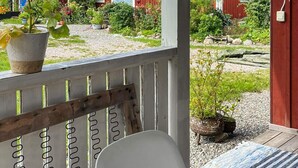 A wooden bench with a white cushion, a potted plant, and a view of a red building with a blue door. - 4 Person Holiday Home in Torpshammar (Torpshammar)