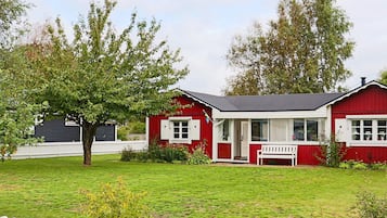 A red building with a white porch and a bench, surrounded by a white picket fence and green grass.