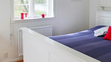 A bedroom with a white bed, a window with a view of trees, and a radiator.