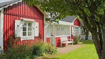A red wooden house with white shutters, a bench, and a garden area.