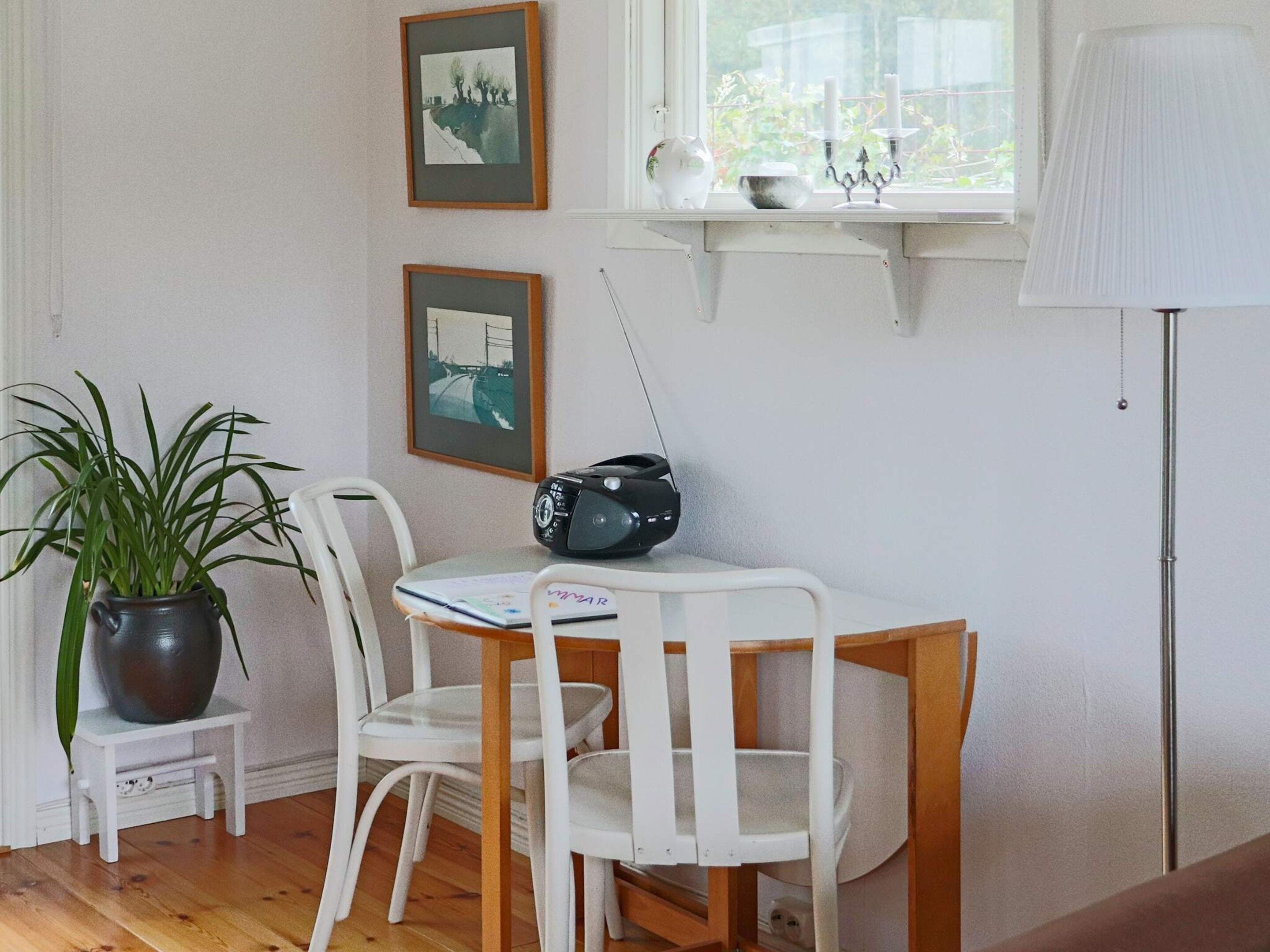 A room with a white table, two white chairs, a potted plant, a radio, and framed pictures on the wall.