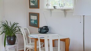 Et værelse med et hvidt bord, to hvide stole, en potteplante, en radio og billeder i rammer på væggen.