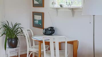 A room with a white table, two white chairs, a potted plant, a radio, and framed pictures on the wall.