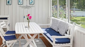 A white wooden deck with a table and chairs, a bench with cushions, and a hanging light fixture.