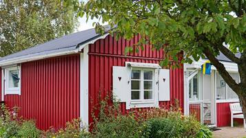 A red building with a white window and shutters, surrounded by greenery and a flag.