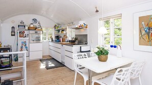 A modern kitchen with white cabinetry, a dining area with white chairs, and a window providing natural light. - 4 Star Holiday Home in Grenaa (Grenaa)