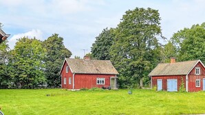 Two red wooden houses with sloped roofs, surrounded by green grass and trees. - 4 Person Holiday Home in Mariestad (Mariestad)