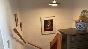 A staircase with a wooden handrail, a framed picture on the wall, a decorative bowl on a cabinet, and a hanging light fixture. - 4 Star Holiday Home in Ebeltoft (Ebeltoft)