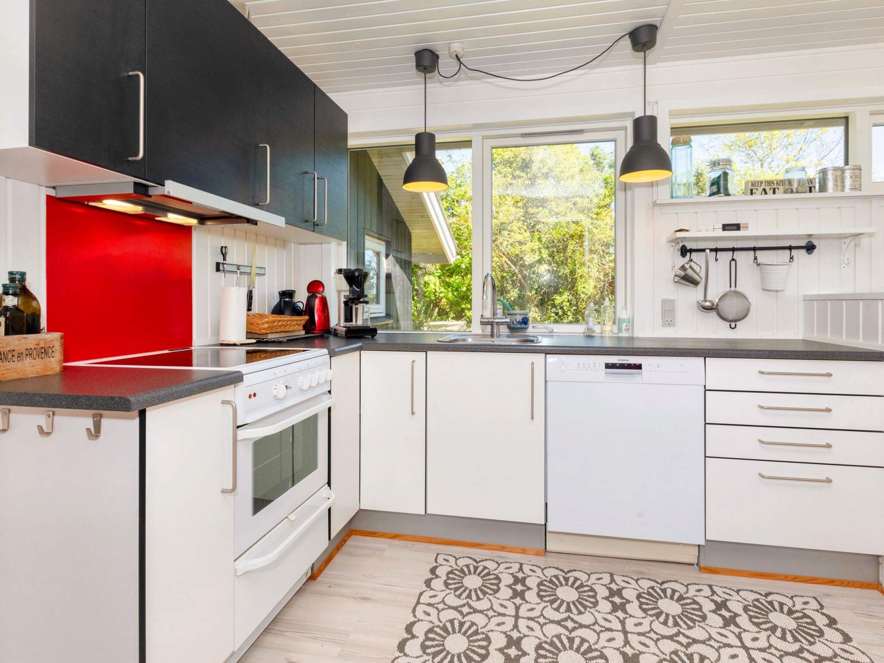 Una cocina moderna con armarios blancos, una pared de acento roja, horno empotrado y un ventanal que proporciona luz natural.