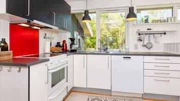 Una cocina moderna con armarios blancos, una pared de acento roja, horno empotrado y un ventanal que proporciona luz natural.