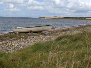 Un barco llamado 'Spectrum' en una orilla pedregosa, con césped y un paisaje arenoso distante.