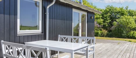 A wooden deck with a white table and bench, a window, and a chimney.
