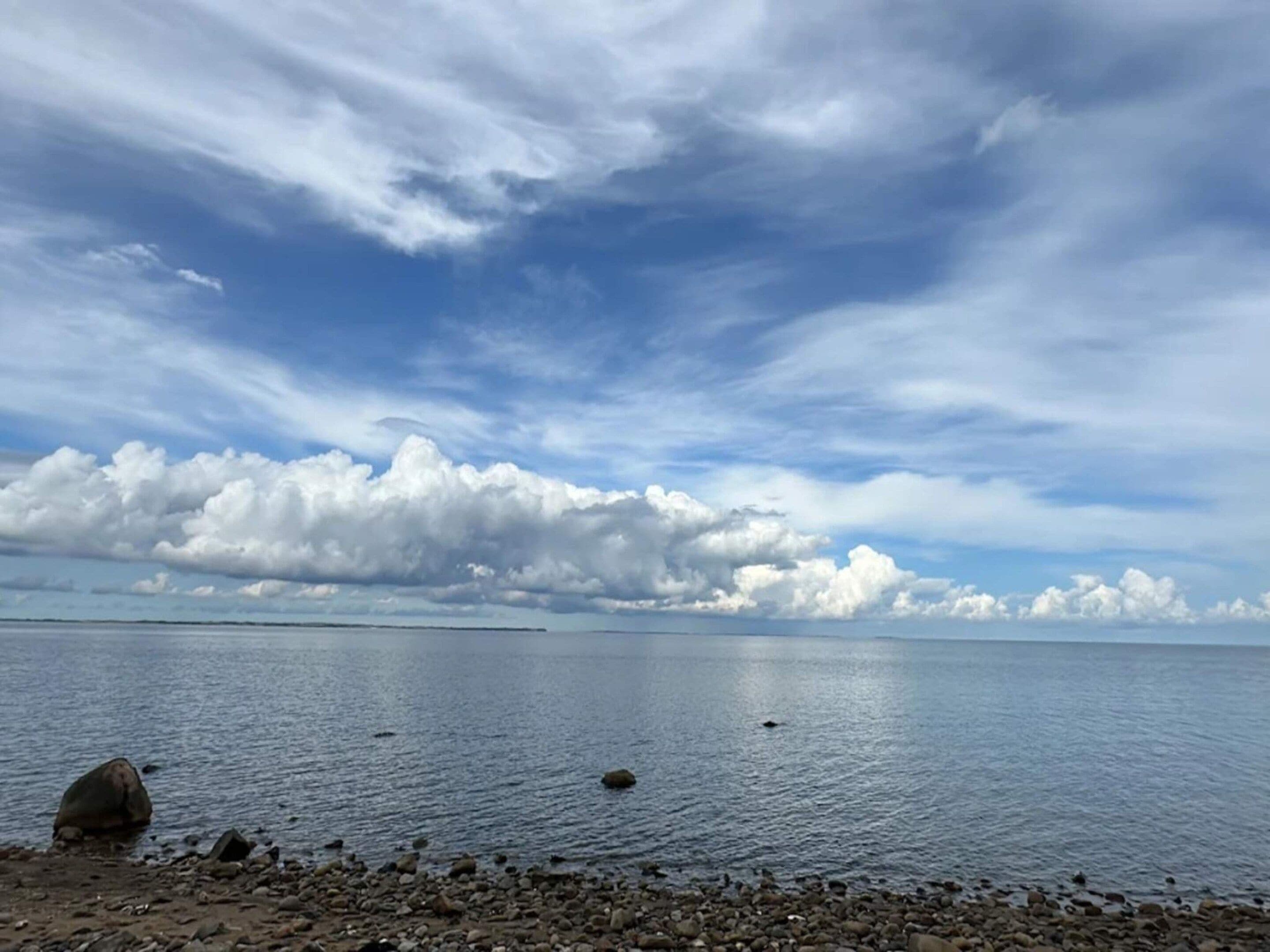 Une étendue d’eau calme, bordée d’une côte rocheuse, sous un ciel partiellement nuageux.