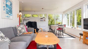 A modern living room with a grey sofa, red rug, wooden coffee table, and a dining area with a table and chairs.