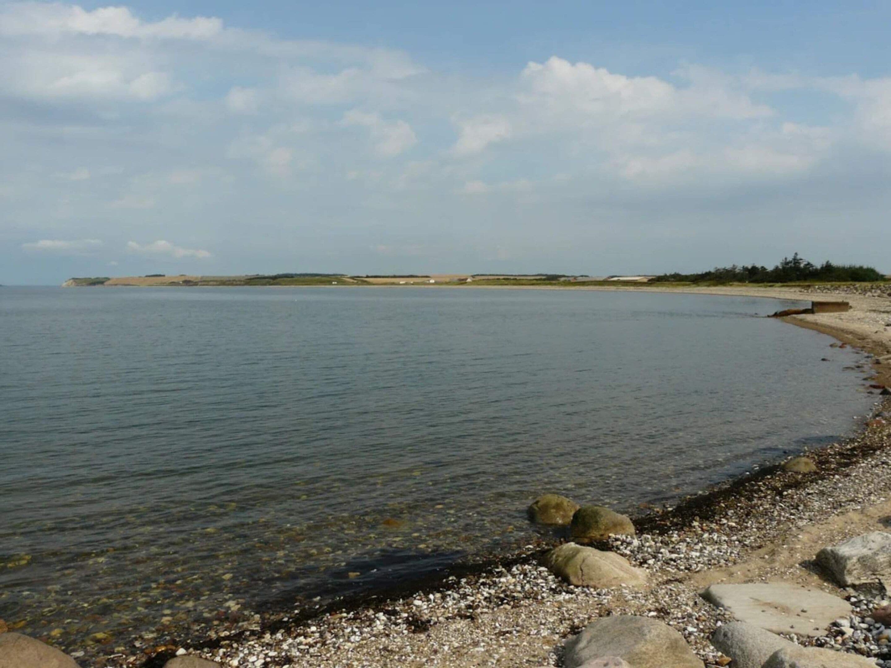 A calm beach with clear water, pebbles, and a distant shoreline.