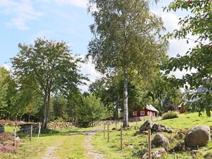 Un paysage rural avec une maison rouge, un mur de pierres et un chemin qui y mène.