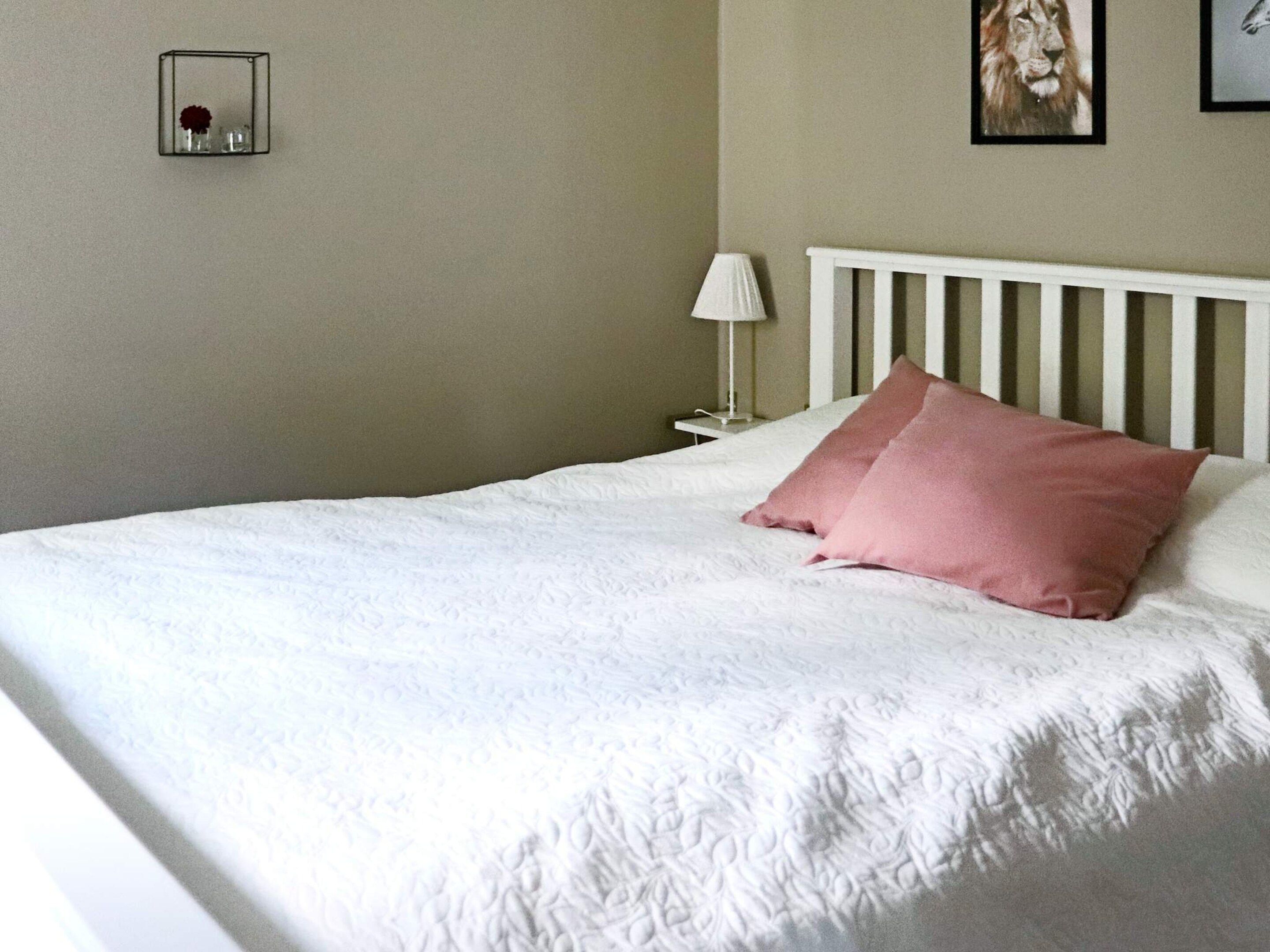 A neatly made bed with a white headboard and a single pink pillow.