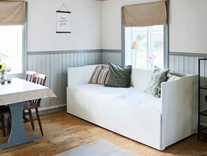 Et hyggeligt rum med en hvid sofa, et spisebord med stole og et vindue med gardiner.