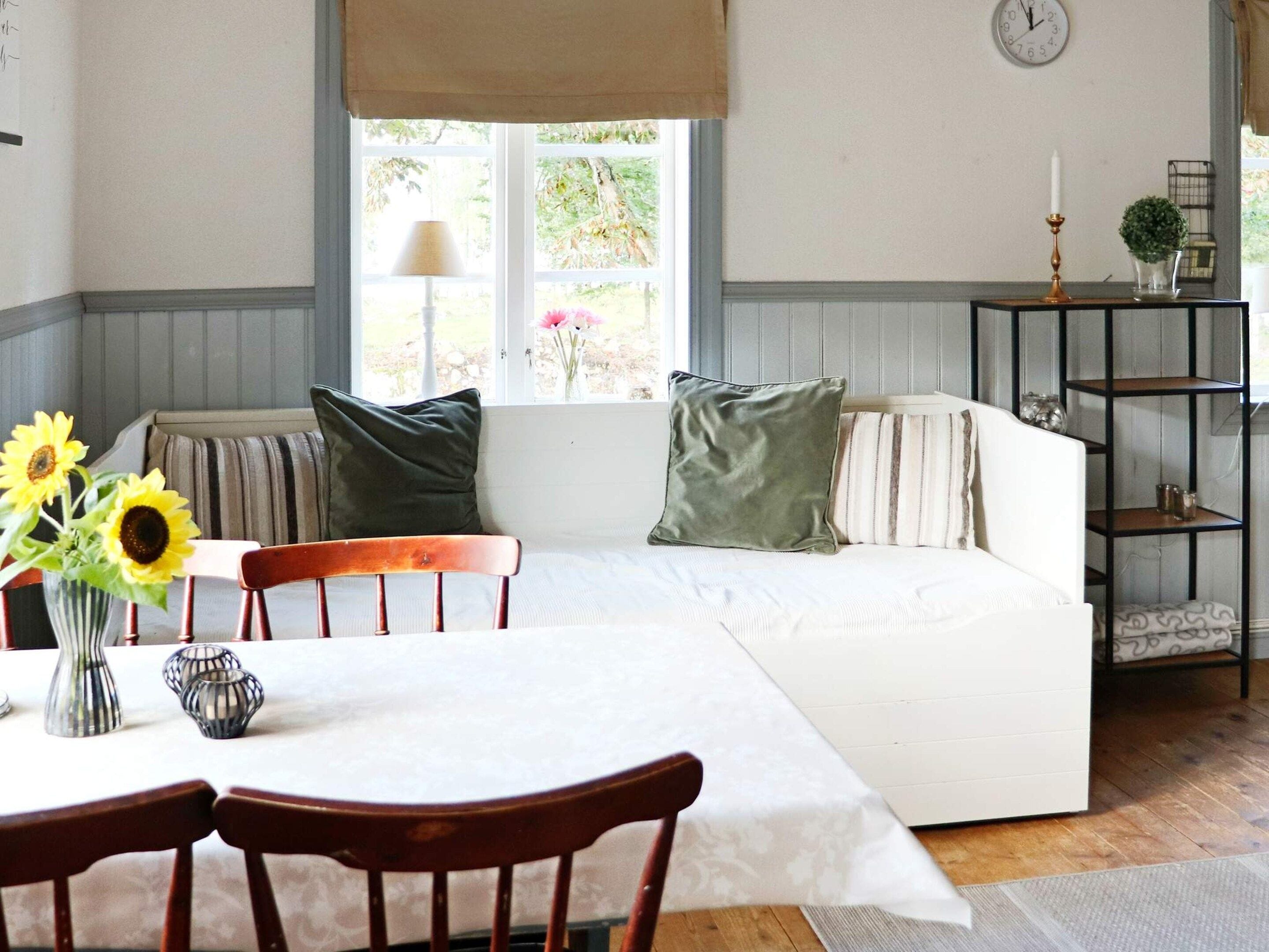 A cozy living room with a sofa, chairs, a dining table, and a window with a view of greenery.