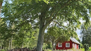A red house with a stone wall and a large tree in front. - 4 Person Holiday Home in Unnaryd (Unnaryd)