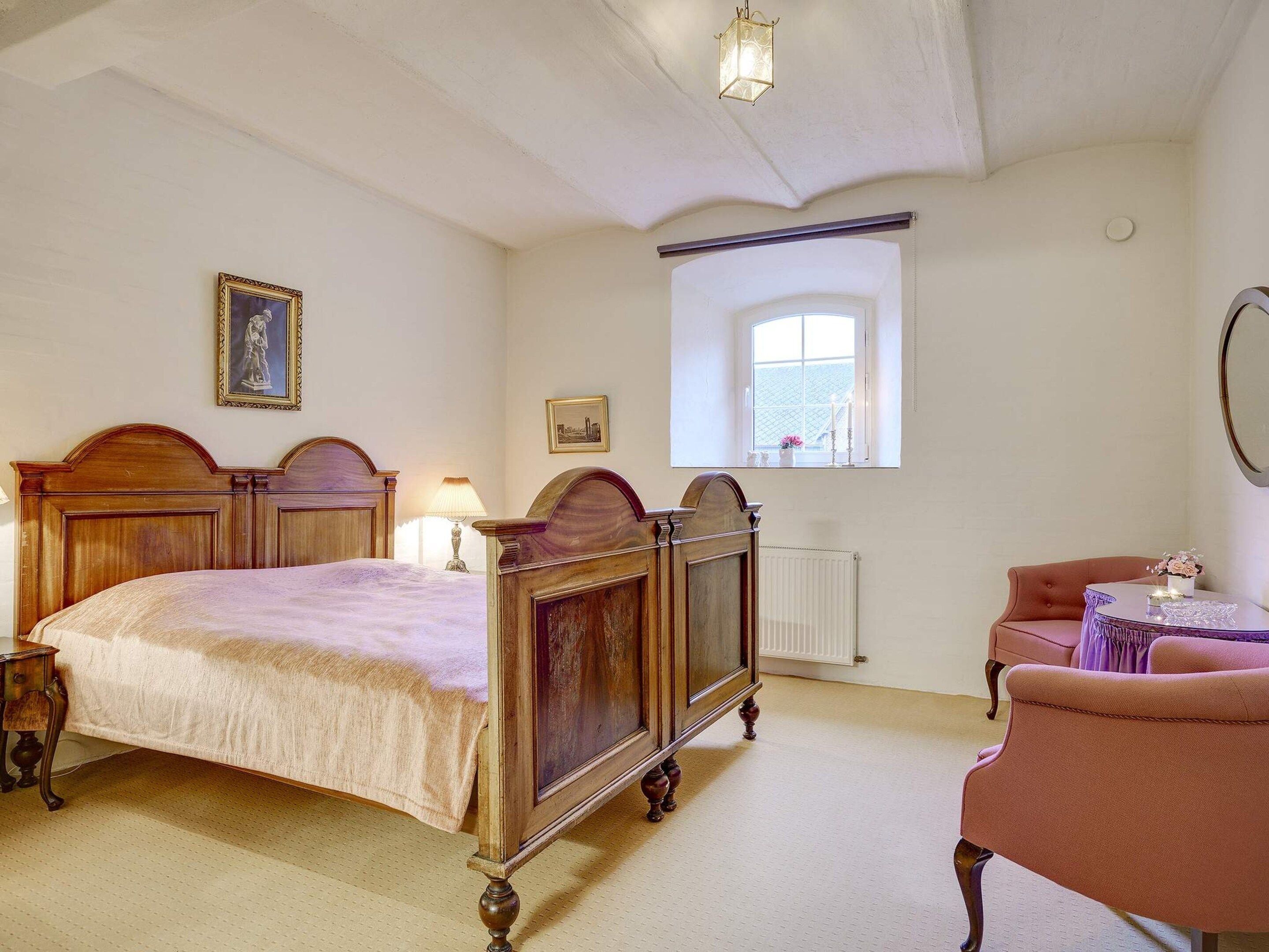 A bedroom with a large bed, a window, a chair, and a small table.