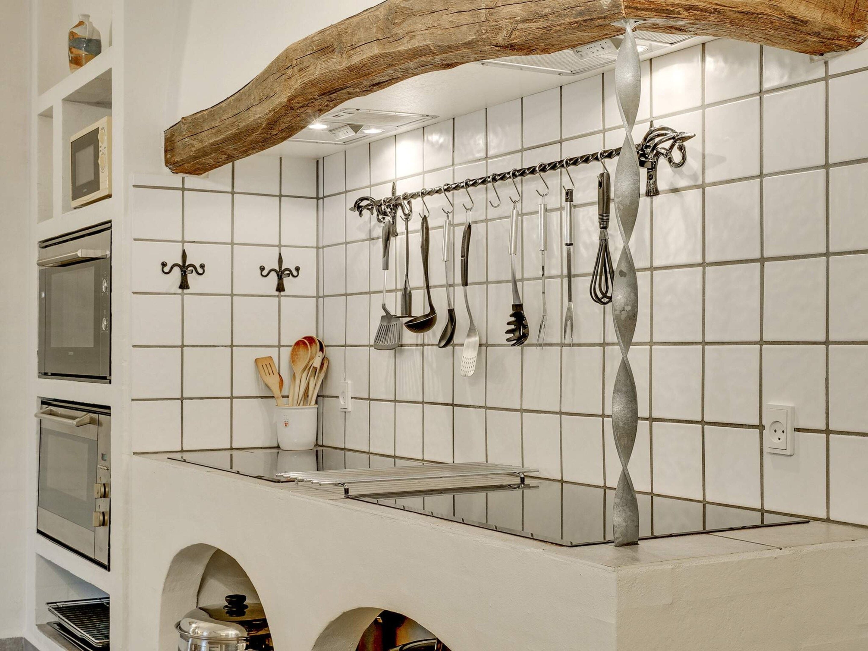 Una cocina con baldosas blancas, utensilios colgantes y una viga de madera sobre la encimera.