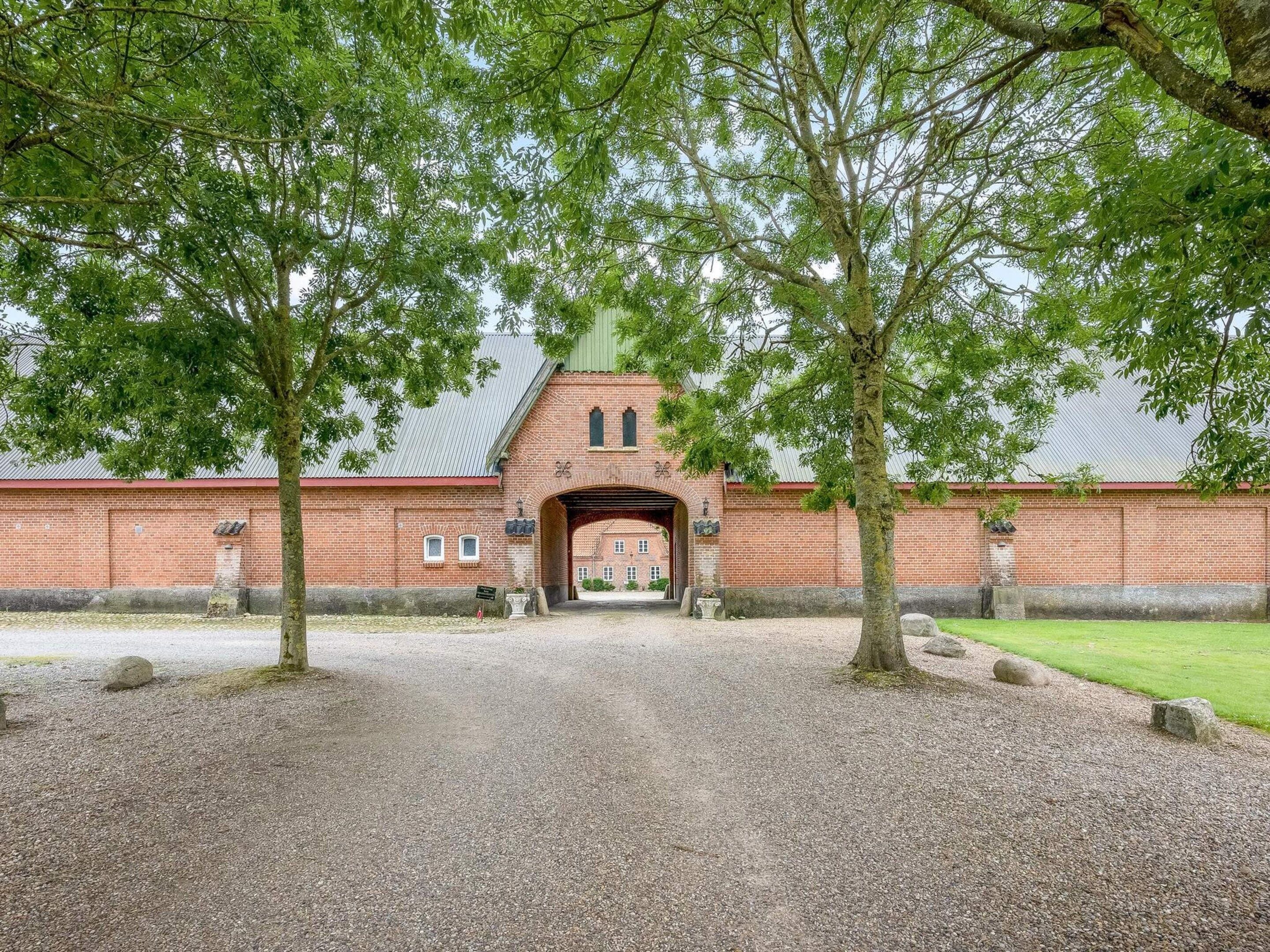 Un bâtiment en briques doté d’une arche centrale, entouré de gravier et d’arbres.