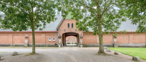 Een gebouw van baksteen met een centrale boog, omgeven door grind en bomen.