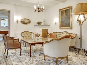 A room with a dining table, chairs, a sofa, a chandelier, wall-mounted lamps, and a fireplace. - 5 Star Holiday Home in Spottrup (Spøttrup)