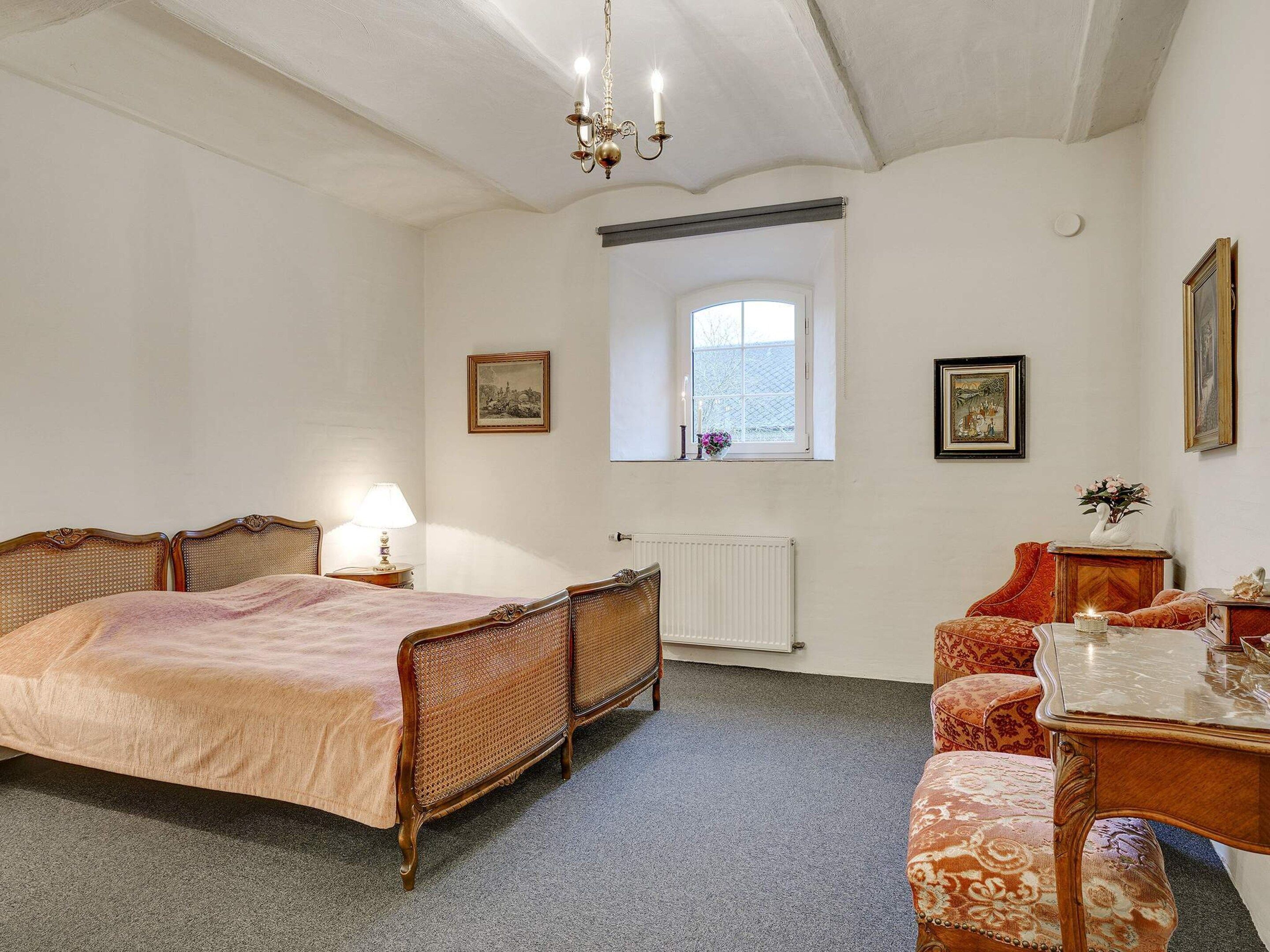 Un dormitorio con cama, escritorio, silla, radiador y ventana.
