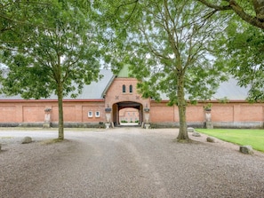 A brick building with a central archway, surrounded by gravel and trees. - 5 Star Holiday Home in Spottrup (Spøttrup)