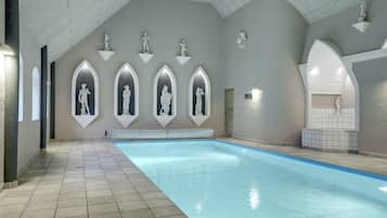 Una piscina interior con arcos que contienen estatuas, suelo de baldosas y techo abovedado.