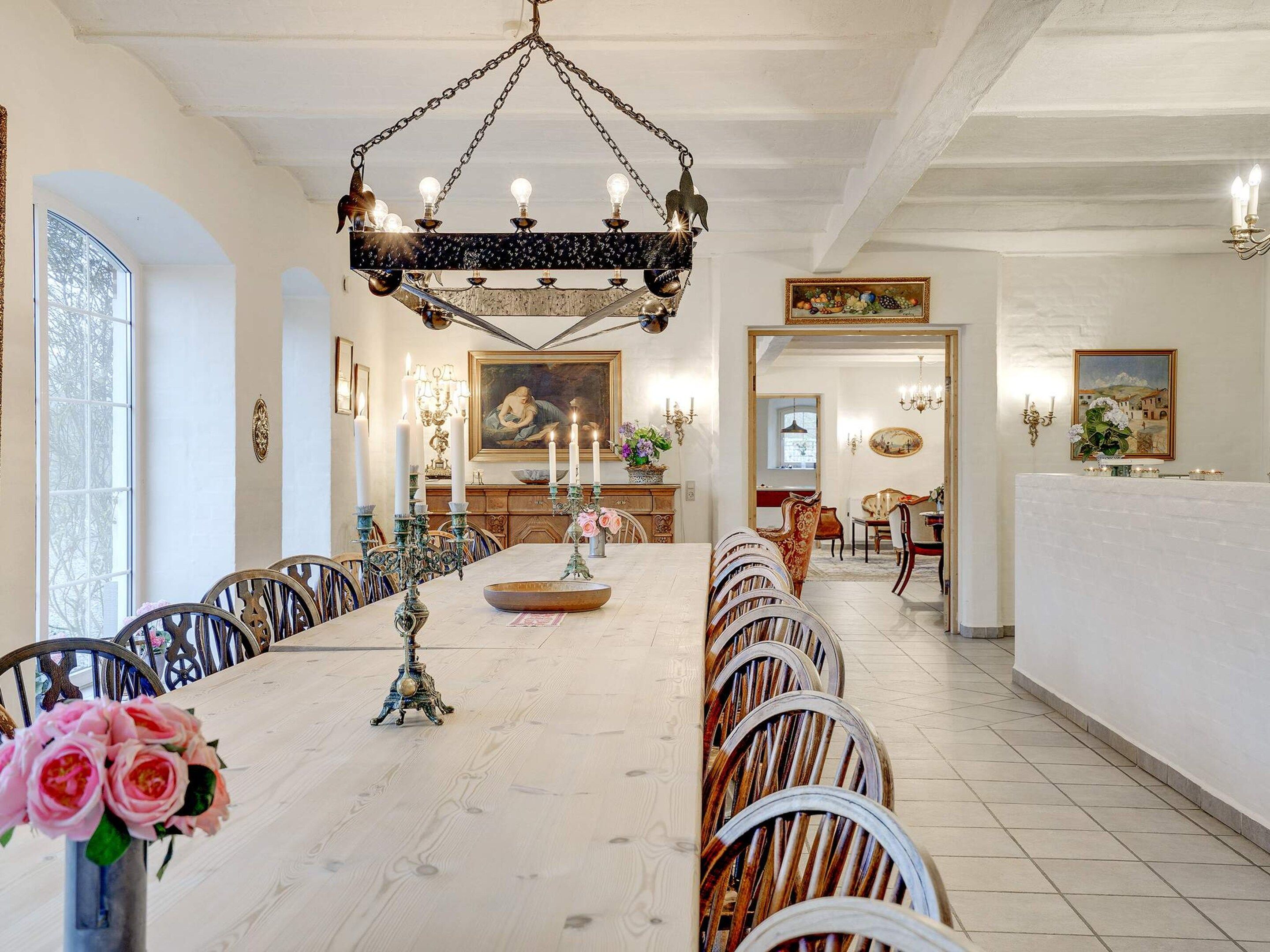 A dining area with a long table, chairs, and a chandelier.