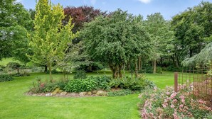 A well-maintained garden with various trees and shrubs, a grassy lawn, and a metal fence. - 5 Star Holiday Home in Spottrup (Spøttrup)