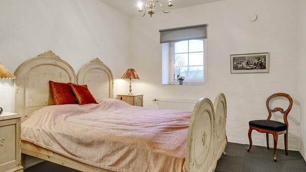 A bedroom with a bed, a nightstand, a chair, a window, and a chandelier. - 5 Star Holiday Home in Spottrup (Spøttrup)