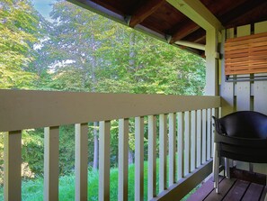 A wooden deck with a railing, a black chair, and a view of a forested area. - 5 Person Holiday Home in Allinge (Allinge)