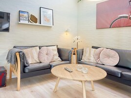 Una sala de estar moderna con un sofá gris, una mesa de centro redonda de madera y un televisor montado en la pared.