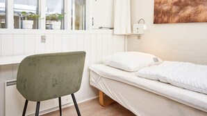 Une pièce comprenant un lit, une chaise, une fenêtre avec des rideaux, un luminaire fixé au mur et un tableau.