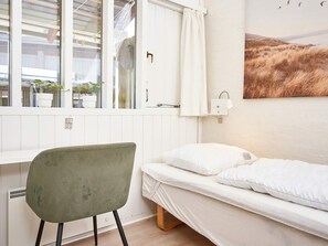 A room with a bed, a chair, a window with curtains, a wall-mounted light, and a painting. - 5 Person Holiday Home in Allinge (Allinge)