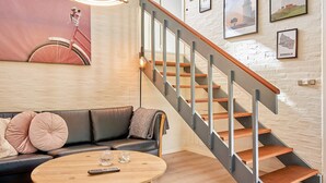 Un salon moderne avec un escalier en bois, un canapé en cuir noir, une table basse ronde en bois et des tableaux encadrés accrochés au mur.