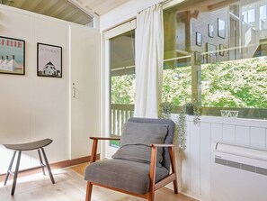 A room with a wooden chair, a small stool, a window with a view of greenery, and a wall with framed pictures. - 5 Person Holiday Home in Allinge (Allinge)