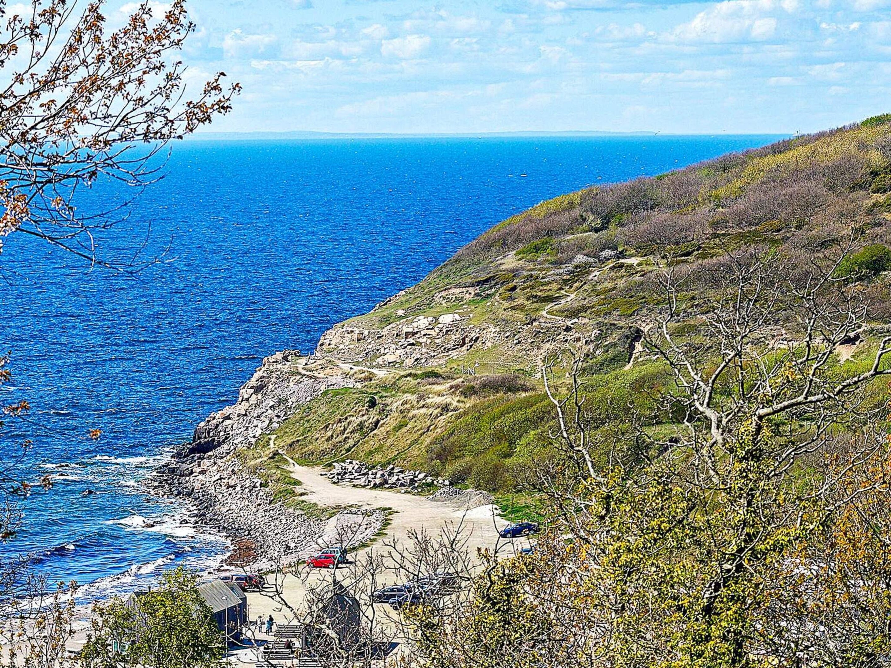 Un paysage côtier caractérisé par une rive rocheuse, un sentier de terre et une végétation clairsemée.