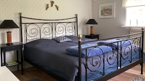 A bedroom with a metal bed frame, two bedside tables with lamps, a patterned wall, a window with curtains, and a framed picture on the wall. - 4 Star Holiday Home in Rimbo (Rimbo)