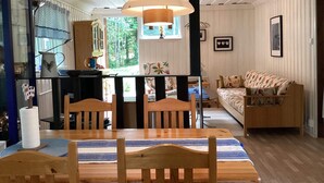 Un salón acogedor con una mesa de comedor de madera, sillas y un sofá. Se ve una ventana con vistas a árboles.