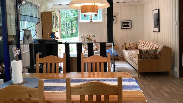 A cozy living room with a wooden dining table, chairs, and a sofa. There is a window with a view of trees outside. - 4 Star Holiday Home in Rimbo (Rimbo)