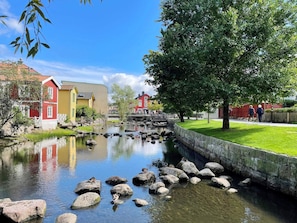 A calm river with rocks, a bridge, and buildings with red and yellow facades.