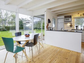 Une cuisine moderne dotée d’un grand îlot central, de meubles blancs et offrant une vue sur le jardin.